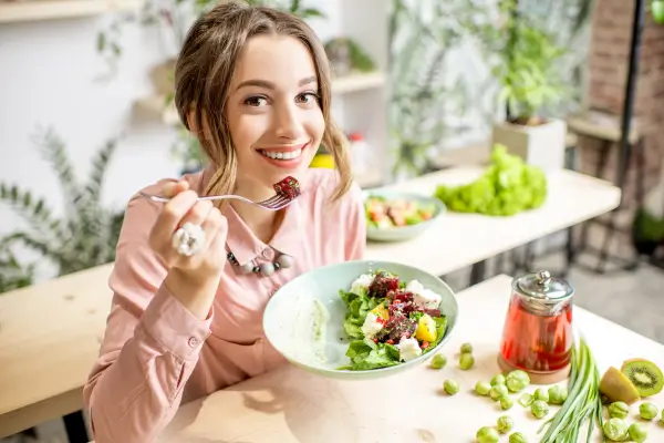 Mulher sorridente apreciando uma salada saudável em ambiente iluminado, destacando como criar uma alimentação saudável sem abrir mão do sabor.