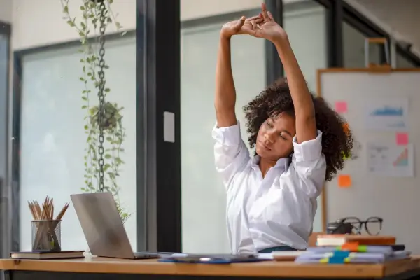 Uma mulher realizando alongamentos no trabalho, exemplificando como melhorar a coluna de forma prática.