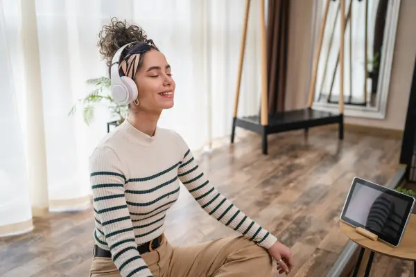 Mulher meditando com fones de ouvido, sentada no chão em um ambiente confortável, representando meditação guiada em casa.